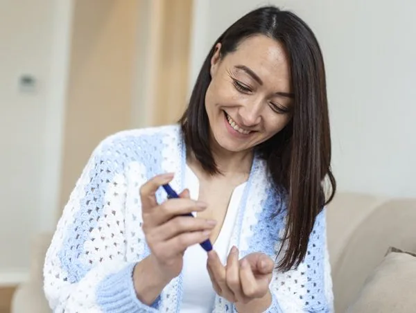 Person using a blood testing device on their finger smiling with neutral colours and background. Diabetes Awareness training,